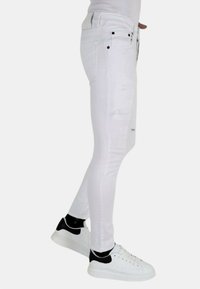 Witte skinny jeans met versleten details, meerdere zakken en zwarte accenten, gestyled met witte sneakers met zwarte accenten.