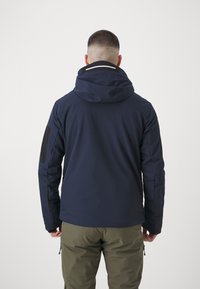Námorně modrá nepromokavá bunda s kapucí, která má černé záplaty na loktech a reflexní prvek na zádech. Texturovaná látka, přiléhavý střih.