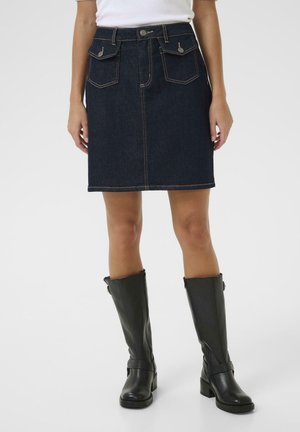 Jupe en denim foncé avec une taille ajustée, deux poches avant et des coutures contrastantes, associée à des bottes en cuir noir montantes.