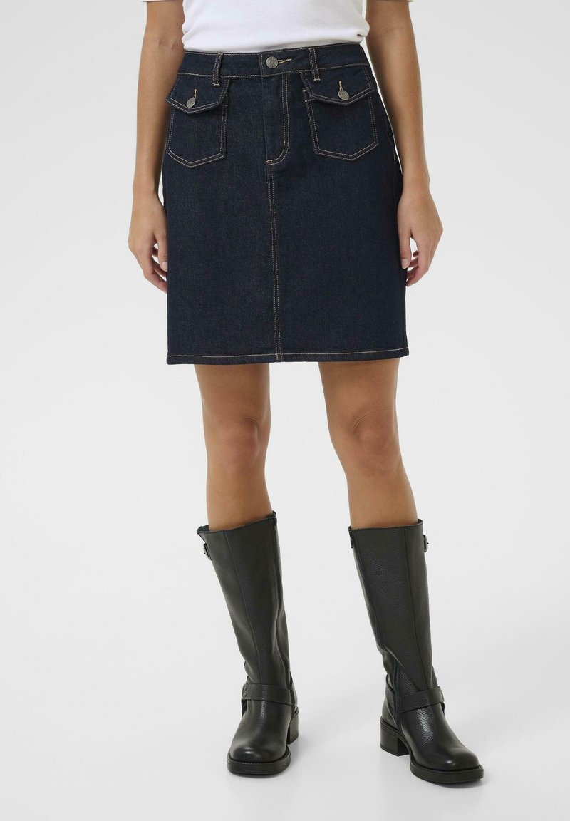 Donkerblauwe spijkerrok met een getailleerde taille, twee voorkeurs en contrasterend stiksel, gecombineerd met zwarte leren laarzen tot de knie.