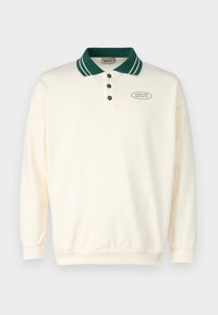 Kremowa polo z długim rękawem, z ciemnozielonym kołnierzykiem i guzikami, z logotypem "Kaotiko Society" na lewej piersi.