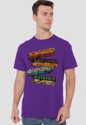 Young man wearing a purple T-shirt with distressed, colorful bands labeled Gryffindor, Hufflepuff, Ravenclaw, and Slytherin.