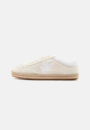 Zapatilla casual beige con textura tejida, cordones blancos, logo "TH" bordado en blanco en el lateral y suela de yute trenzado sobre fondo blanco.