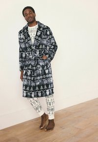 Halat de baie cu un model alb-negru, cu animale și copaci, legat în talie. Purtați peste o pereche de pantaloni de pijama cu un model deschis la culoare.