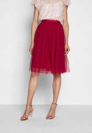 Red tulle skirt with a voluminous design, lined underneath, features a gathered waistband. Paired with a light, embroidered top and strappy sandals.