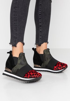 Ben iført sorte jeans med frynset kant og sorte slip-on kilehælssneakers med rød leopardprint og grøn camouflage detaljer.