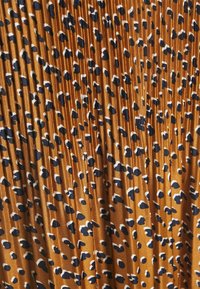 Faltenstoff in einem warmen Rostton mit einem Leopardenmuster aus schwarzen und weißen Flecken. Glatte Textur, leichtes Material.
