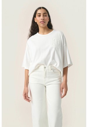 Weißes, übergroßes T-Shirt mit Rundhalsausschnitt und einem strukturierten Logo-Patch auf der Brust, kombiniert mit weißen, hoch taillierten, weiten Jeans.