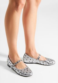 Strieborné baletky s okrúhlou špičkou, zdobené kovovými očkami a pásikom cez priehlavok. Hladký povrch a nízky opätok.