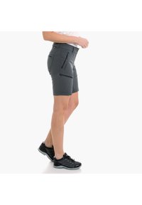 Pantalones cortos grises de tejido ligero con múltiples bolsillos con cremallera, corte ajustado y longitud hasta la rodilla. Combinados con zapatillas deportivas negras.