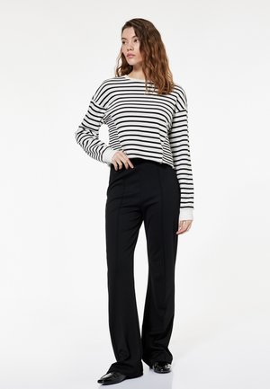 Zwart-wit gestreepte sweatshirt met ronde hals, gecombineerd met hoogstaande, op maat gemaakte zwarte broek en glanzende zwarte schoenen.