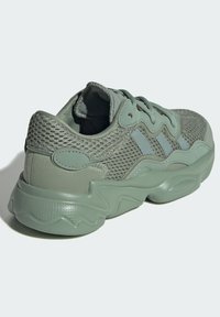 Green mesh sneaker featuring a textured rubber sole, three light blue stripes, and a padded collar for comfort. Smooth finish on the heel.