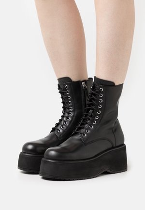 Bottines en cuir noir avec un bout arrondi, un laçage sur le devant, une fermeture éclair sur le côté et une semelle épaisse. Texture lisse avec des accents minimaux.