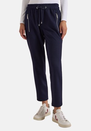 Marineblaue Jogginghosen mit elastischem Bund und Kordelzug, vordere Reißverschlusstaschen, getragen mit weißen Sneakers und einem weißen Langarmshirt.