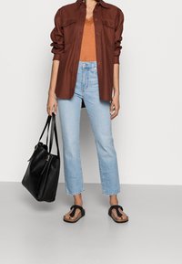 Brun oversized skjorta, orange topp, ljusblå raka jeans, svart tote bag och svarta flip-flops med texturerad sula.