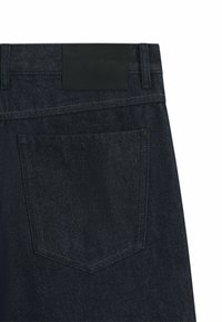 Jeans in denim scuro con un'etichetta in pelle in vita, dotati di una tasca posteriore e cuciture a contrasto. Morbida texture, materiale resistente.