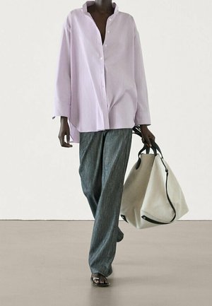 Person wearing loose lavender button-up shirt and gray wide-leg pants, carrying a large beige tote bag with black handles.
