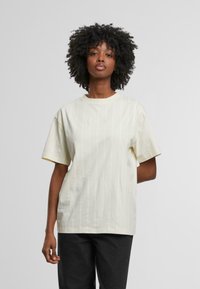 Camiseta de manga corta amarilla claro con rayas blancas verticales y un escote redondo. Presenta un sutil detalle bordado en el pecho.