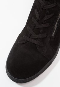 Baskets en daim noir avec bout rond, lacets noirs, fermeture éclair métallique sur le côté et semelle en caoutchouc texturée, vues de dessus à l’avant.