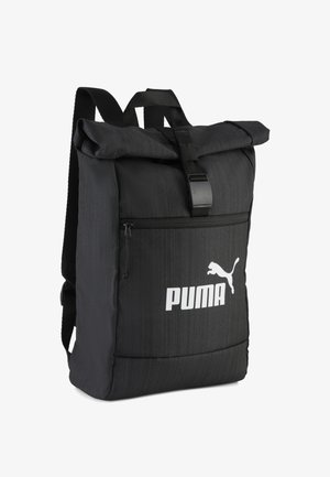 Sac à dos noir à rabat enroulable en tissu texturé, doté d'une poche zippée à l'avant et d'un logo blanc. Sangles ajustables et fermeture à boucle robuste.