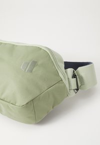 Borsa a vita in tessuto verde chiaro, con una texture e un design elegante, cinturino regolabile e un discreto dettaglio del logo. Chiusura con cerniera per una custodia sicura.