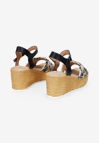 Sandalias de cuña de cuero negro con parte superior de tejido de leopardo, suela natural texturizada y cierre de hebilla en la correa del tobillo.
