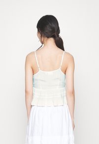 Camisola plissettata azzurro chiaro e crema con spalline regolabili e orlo svasato. Presenta un delicato pizzo decorativo in vita.