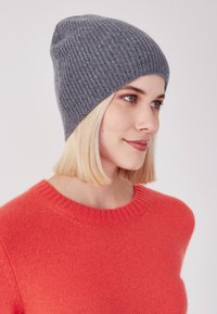 Beanie a costine grigia realizzata in materiale morbido, con design affusolato. Indossato con un vivace maglione rosso, evidenziando il contrasto di colore.