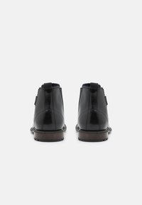 Botines de cuero negro con un acabado liso, tacón bajo y suela marrón en contraste. Presentan paneles laterales elásticos y tiradores en la parte posterior.