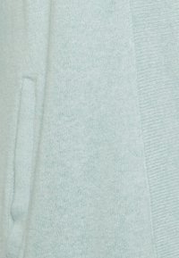 Hellblauer Strickpullover mit einer Vordertasche und geripptem Rand, der ein weiches, kuscheliges Material zeigt.