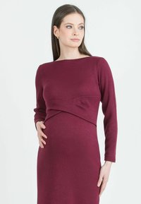 Těhotenské šaty v hluboké burgundské barvě, dlouhé rukávy, přiléhavý silueta s přehozením v pase, jemná pletenina.