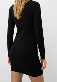 Robe noire à manches longues, cintrée, en matière tricotée douce. Dotée d'un ourlet et de poignets côtelés, avec une texture lisse sur toute la surface.