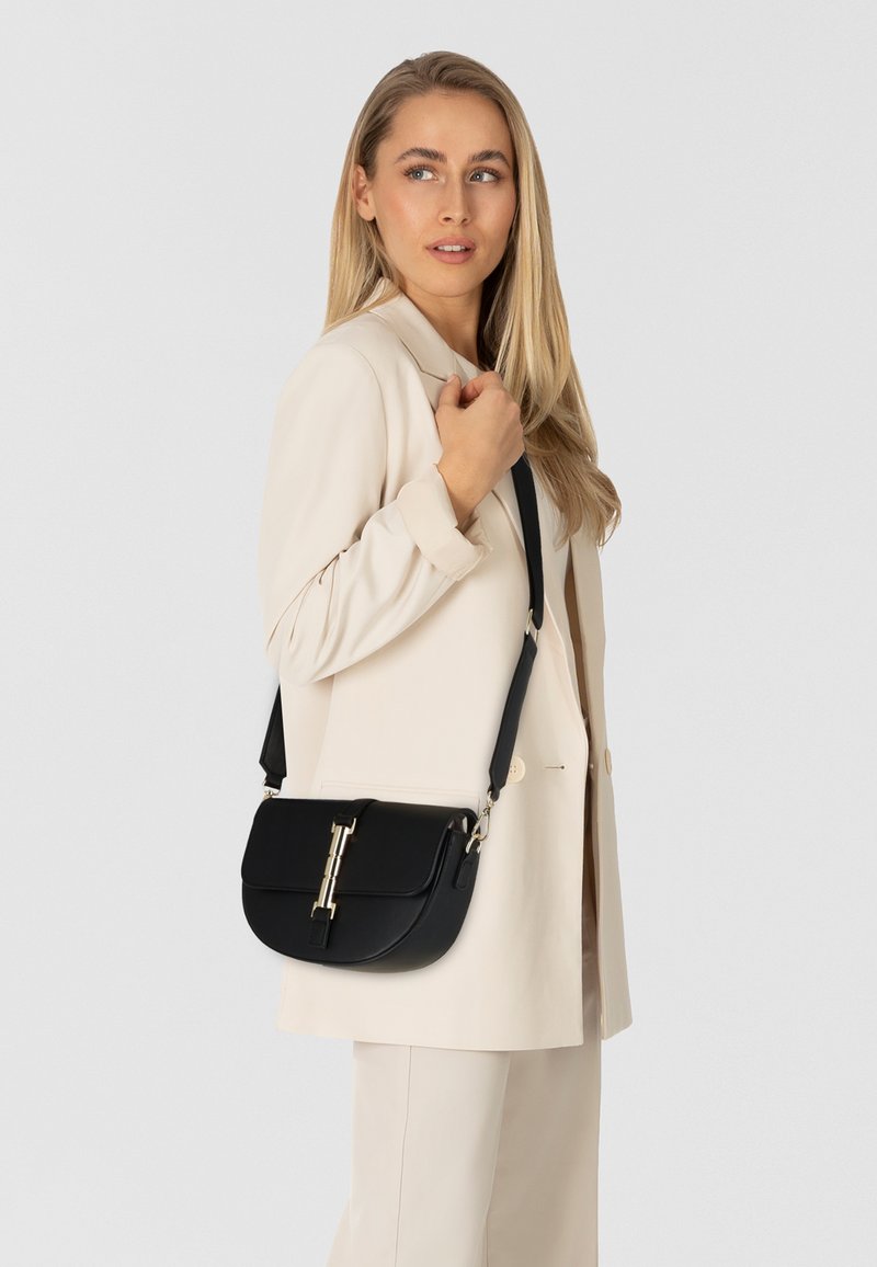 Borsa a tracolla in pelle nera con una texture liscia, hardware in tonalità oro e una forma arrotondata e strutturata. Incluso cinturino regolabile.