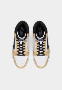 Ζευγάρι από λευκά, μπεζ και μαύρα sneakers υψηλού πάνω μέρους με μαύρα κορδόνια, απεικονισμένα από πάνω σε λευκό φόντο.