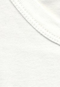 Primer plano de una tela de punto blanca con costuras detalladas a lo largo de un borde curvado.