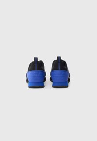 Pair of black and blue athletic sneakers shown from the back with GA logo embossed on the blue heel counter.