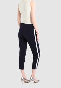 Granatowe spodnie z białymi bocznymi paskami, w skróconej długości, z elastycznym paskiem w talii, zestawione z metalicznymi butami na obcasie. Wzorzysty sweter