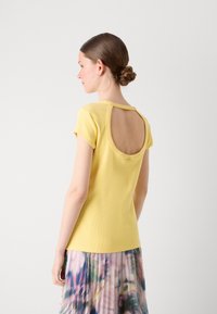 Haut jaune côtelé à manches courtes avec une large découpe circulaire au dos. Associé à une jupe plissée multicolore. Texture lisse.