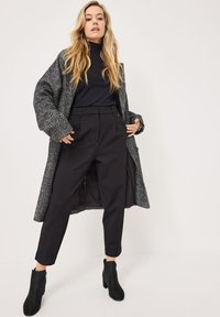 Gray houndstooth coat, ribbed black turtleneck, black tailored trousers, and black ankle boots. Soft textures and structured shapes.