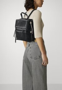 Schwarzer Leder-Rucksack mit geripptem Design, doppeltem Frontreißverschluss und dekorativen Akzenten. Verfügt über verstellbare Träger und ein kompaktes Design.