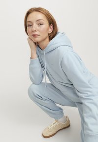 Felpa blu chiaro e pantaloni abbinati in un tessuto soffice. Presenta lacci, polsini a coste e sneakers beige con accenti crema.