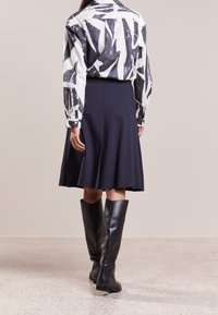 Svart och vit mönstrad skjorta, marinblå utsvängd kjol och höga svarta läderstövlar. Slät tyg med kontrasterande färger och rena linjer.