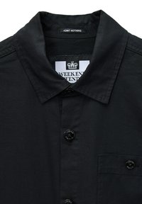 Schwarzes kurzärmliges Hemd mit spitzem Kragen, ausgestattet mit einer durchgehenden Knopfleiste, Brusttasche und einem Etikett, das "ADMIT NOTHING" liest.