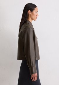 Przycięta, oliwkowo-zielona skórzana kurtka z kołnierzem i guzikami, z długimi rękawami i gładką teksturą.