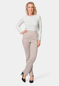 Pantalons beige ajustés avec un devant bouton et des passants de ceinture, associés à un haut blanc à manches longues. Portés avec des chaussures à talons hauts noires.