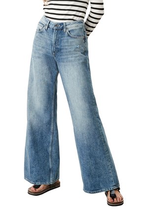 Femme portant un jean large bleu clair et un haut à manches longues rayé, assortis à des sandales à plateforme montrant des orteils vernis.