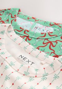 Deux hauts à manches longues ; l'un vert menthe avec des motifs de cocktails et de rubans, l'autre beige avec des nœuds verts et des accents rouges. Les deux présentent des cols côtelés.