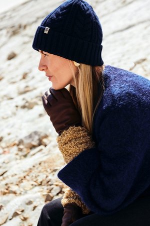 Marine gebreide beanie, donkeren leren handschoenen en een gestructureerde blauwe buitenkleding met een fuzzy tan accent; profielweergave tegen een neutrale achtergrond.