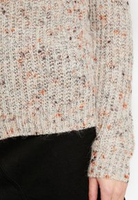 Pletený svetr s tečkovaným vzorem v krémové, hnědé a oranžové barvě. Má žebrovaný lem a manžety, vyrobeno z texturované látky.