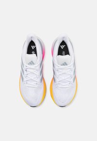 Scarpe sportive bianche con tomaia in mesh, tre strisce grigie, soletta nera, suola in gradiente che passa dal rosa al giallo e lacci bianchi piatti.
